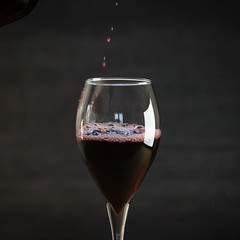 Pouring red wine into the glass against wooden background