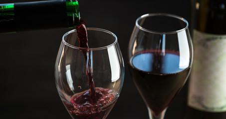 Pouring red wine into the glass against wooden background
