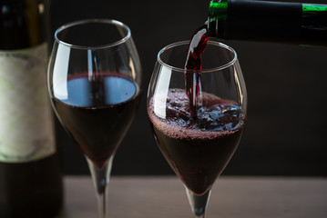 Pouring red wine into the glass against wooden background