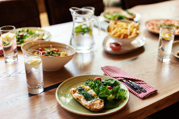 Plates with meals, pitcher and glasses of homemade lemonade on dinner table