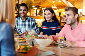 Happy friends having dinner at table with dishes of food and glasses of lemonade in cafe