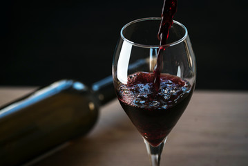 Pouring red wine into the glass against wooden background