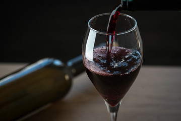 Pouring red wine into the glass against wooden background