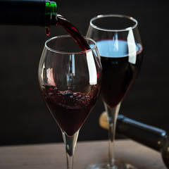 Pouring red wine into the glass against wooden background
