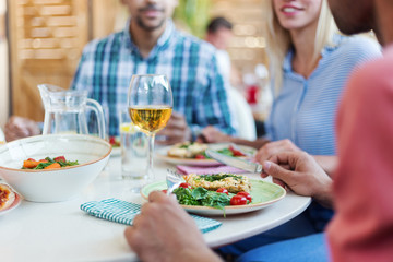 Close-up of fresh healthy dishes and glass of wine on dining table and defocused friends having dinner in restaurant