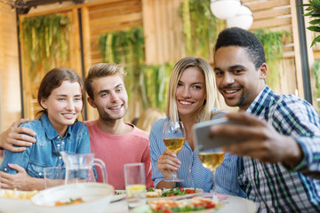 Two young couple having dinner in restaurant together and taking selfie on smartphone