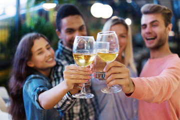 Four young people clinking glasses of wine and lemonade celebrating their friendship at party