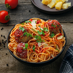 Delicious spaghetti pasta with meatballs and tomato sauce in a bowl. Traditional American Italian food on a rustic wooden table.