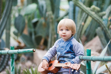 Three years blond boy holding ukulele instrument