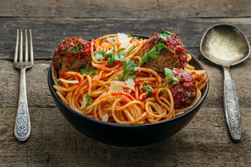 Delicious spaghetti pasta with meatballs and tomato sauce in a bowl. Traditional American Italian food on a rustic wooden table.