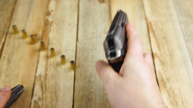 Human unloads magazine from a traumatic pistol on a wooden background.