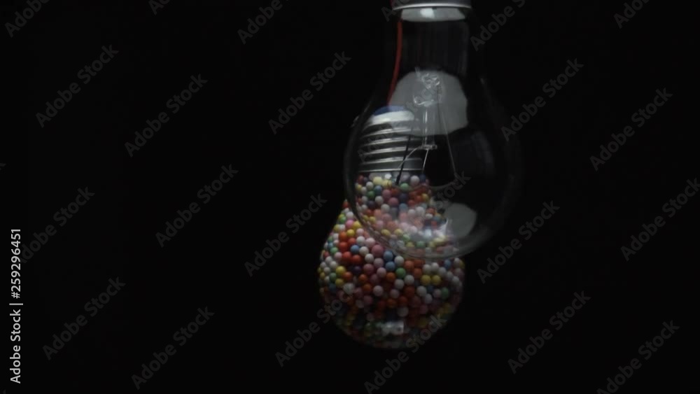 Poster lightbulb filled with colored ball black background. macro view.