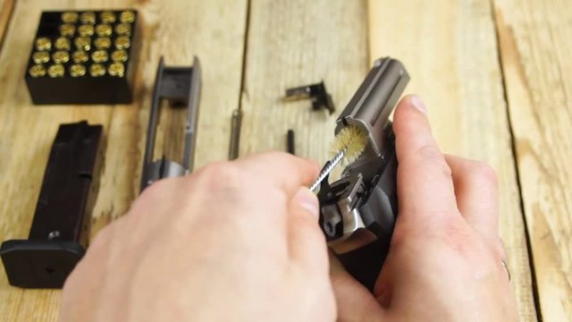 Human cleans the barrel of a disassembled pistol on a wooden background.