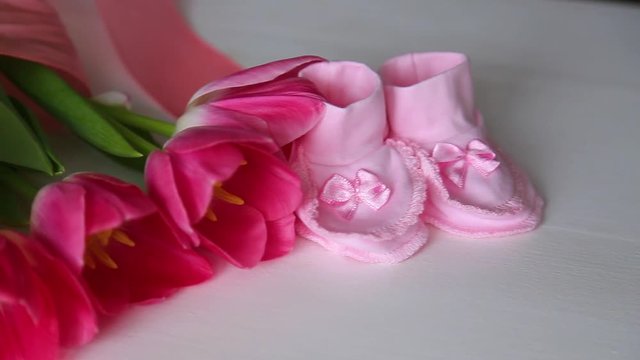 Closeup view of new pink small cute booties standing near bouquet of tulips isolated on white background. Real time full hd video footage.