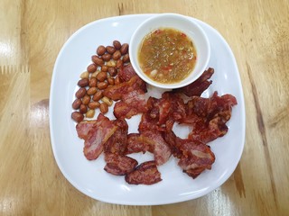 Top view of fried bacon and peanuts with spicy sauce in white plate on wooden table in restaurant