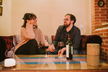 a couple looking at each other while they are sitting on the sofa in a cozy living room where there is a small table with wine glasses