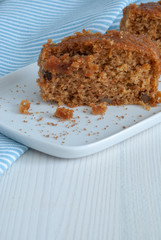 Vertical close-up of carrot cake with nuts on white plate. On white wooden background and blue kitchen cloth with white stripes with copy space