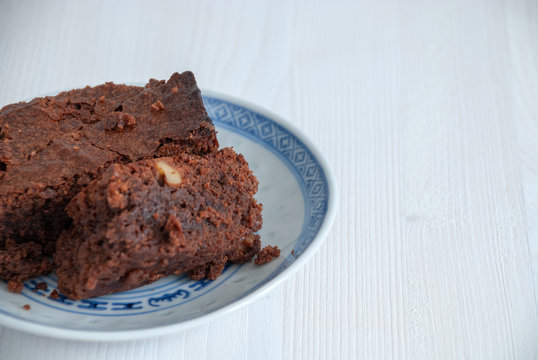 Horizontal close-up of brownie in blue and white dish. On white wooden background with copy space