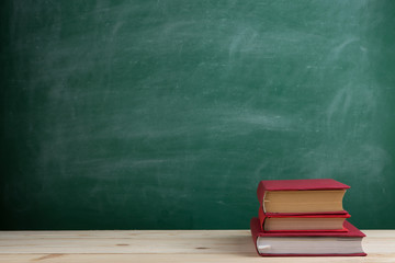 Education and reading concept - group of colorful books on the wooden table in the classroom, blackboard background