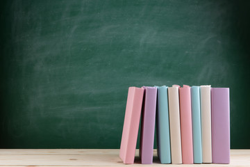 Education and reading concept - group of colorful books on the wooden table in the classroom, blackboard background