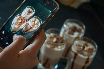 An Indian Woman's hand taking photos of milkshake in glass on her mobile phone.