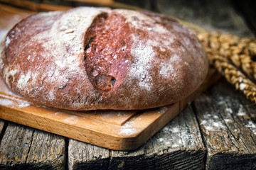 Round bread and wheat ears on the old wooden table