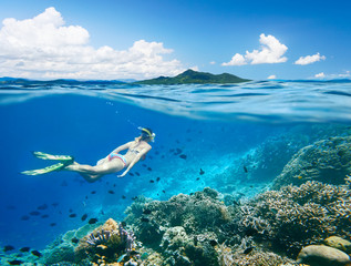 Woman swims around a coral reef surrounded by a multitude of fish on the background Islands..North Sulawesi, Indonesia. - obrazy, fototapety, plakaty