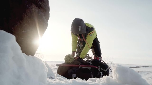 Sitting on the snowy ledge of the mountain, the climber checks the integrity of your backpack, pack rope, hooks, and mounts