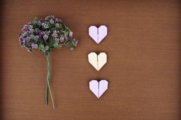 Creative layout made of purple flowers bouquet and an origami paper heart isolated on wooden texture background. Flat lay, top view. Love concept