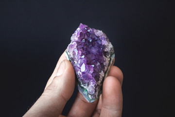 druse of natural untreated violet crystals of amethyst on a piece of rock lies on the palm of your...