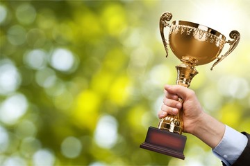 Hands holding golden trophy on light background
