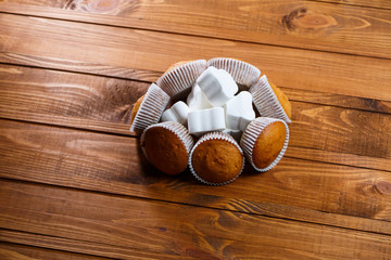 Homemade muffins in paper wrap with marshmallows on wooden board