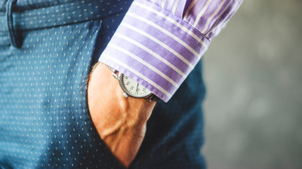 Close-up of Male Hand in Pants Pocket with Elegant Wristwatch. Caucasian Businessman in Striped Shirt Wearing Stylish Dress Watch. Fashion and Punctuality Concept