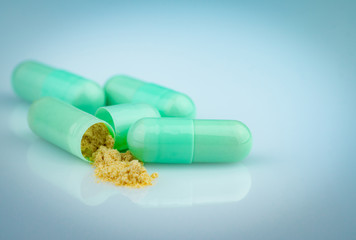 Group of green capsule and open one capsule to show yellow powder of herbal medicine on gradient...