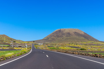 Spain, Lanzarote, Bolt upright road through green fields to volcanic mount monte corona volcano