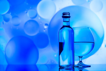 transparent glass and bottle with water and oily drops on azure background 