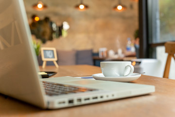 Cup of coffee with laptop on table  in coffee shop.