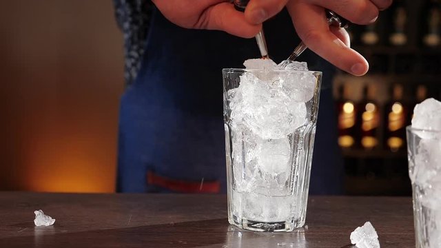 Bartender hands pouring two cocktail ingredients simultaneously on the ice cubes - close up, slow motion of the two pourer nozzles filling the glass