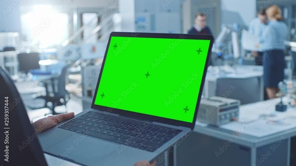 Fototapete Engineer Holds Green Mock-up Screen Laptop Computer. In the Background Team of Industrial Engineers Working with Functional Robot Arm in Modern Bright Research Facility