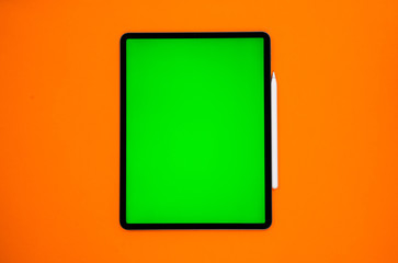 new tablet on a Orange background with a keyboard and pen, and green screen top view