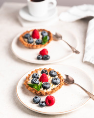 homemade tartlets with blueberries and raspberries on a light marble backdrop, overexposed