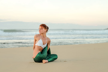 Fototapeta na wymiar Amazingly flexible yoga instructor doing some stretches on the beach