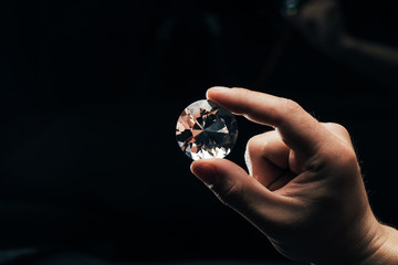 partial view of man holding big clear shiny diamond on black background