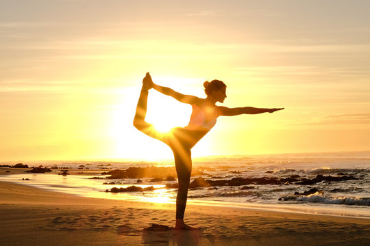 An awesome yoga instructor does some poses on the beach with the sunrise