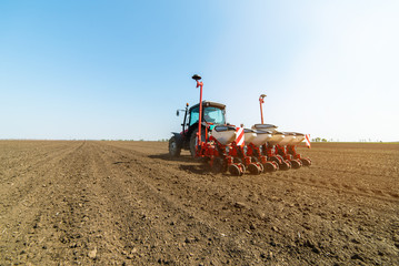 Fototapeta premium Farmer with tractor seeding sowing crops at agricultural field
