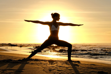 A fantastic yoga instructor does some stretches and poses on the beach with the sunrise