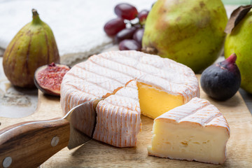 Round piece of French cheese Fleur Rouge made from cow milk served as dessert with fresh figs and pears