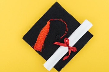 Top view of academic cap and diploma with red ribbon isolated on yellow