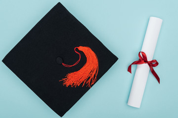 Top view of academic cap and diploma on blue surface