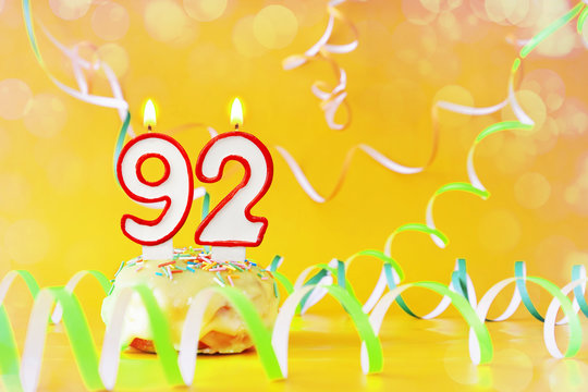 Ninety two years birthday. Cupcake with burning candles in the form of number 92. Bright yellow background with copy space